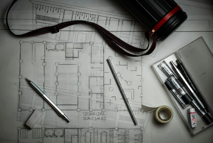 Architectural blueprints with drafting pencils, a metal ruler, and a storage tube